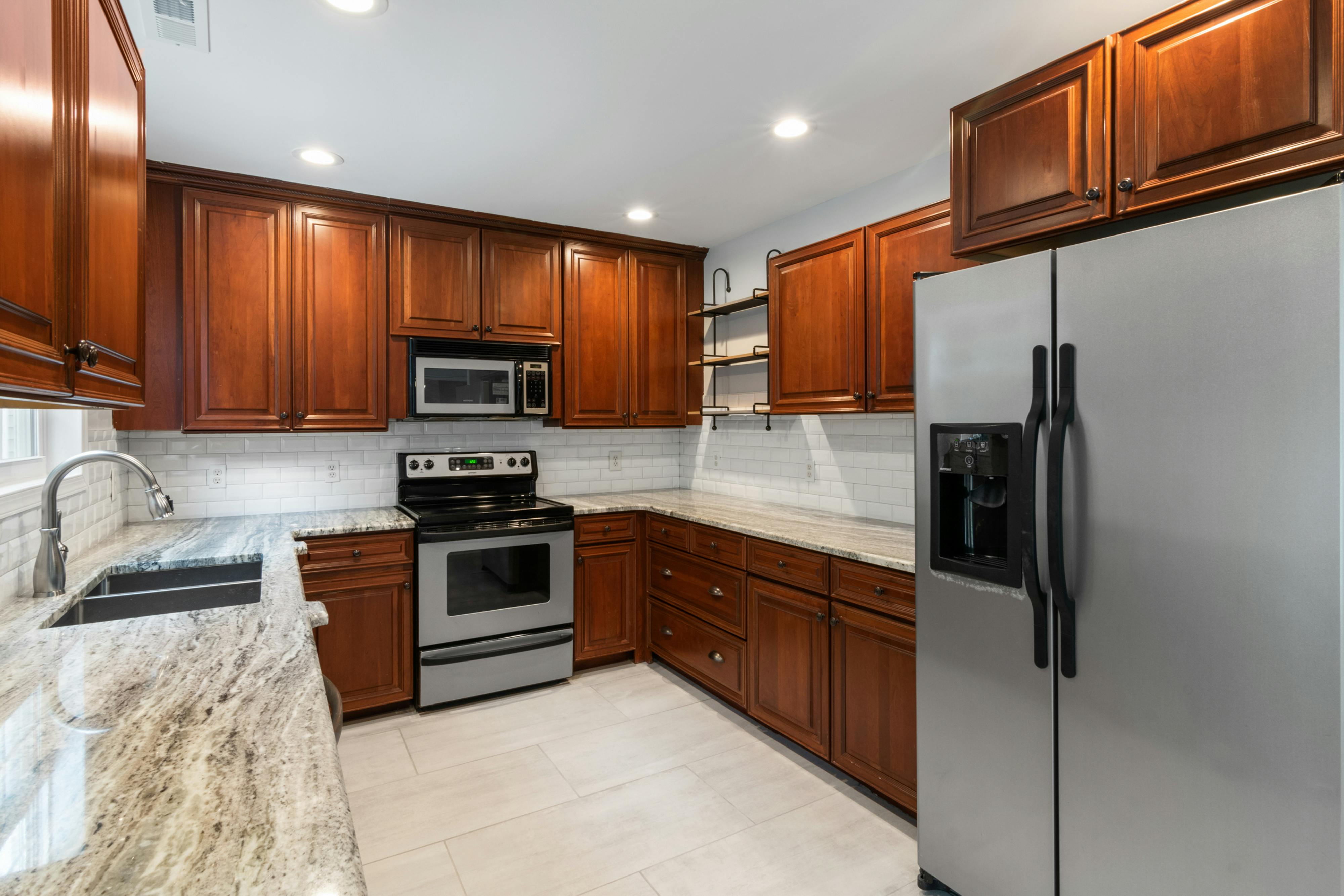 Cherry wood cabinet kitchen remodel with granite countertops, ceramic tile flooring, subway tile backsplash, and recessed lighting.